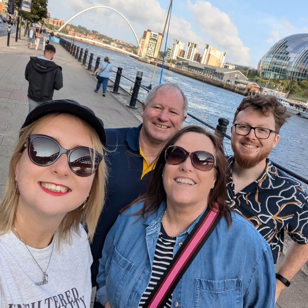 Smiling group taking a selfie by the River Tyne during a Newcastle treasure hunt tour, with the Millennium Bridge and Sage Gateshead in the background